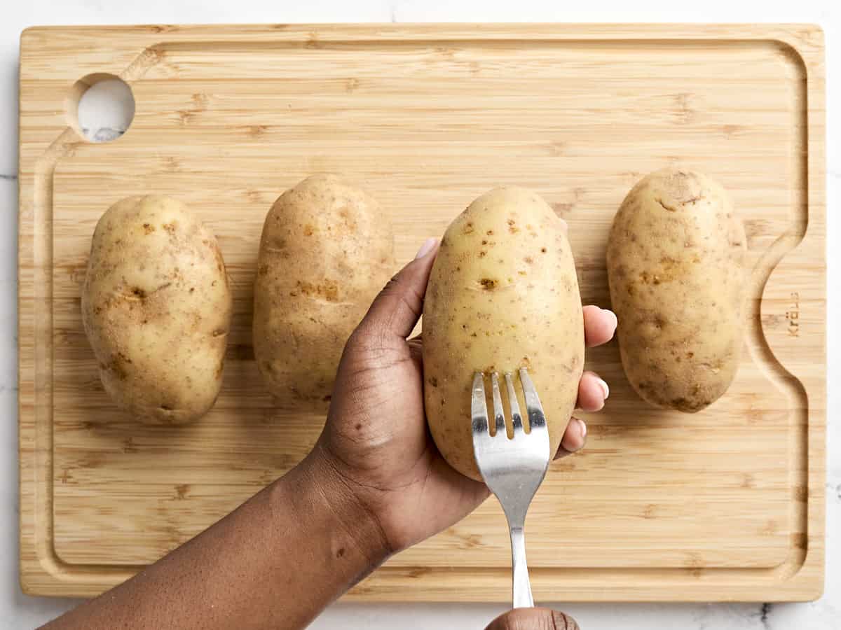 Four russet potatoes being poked with a fork.