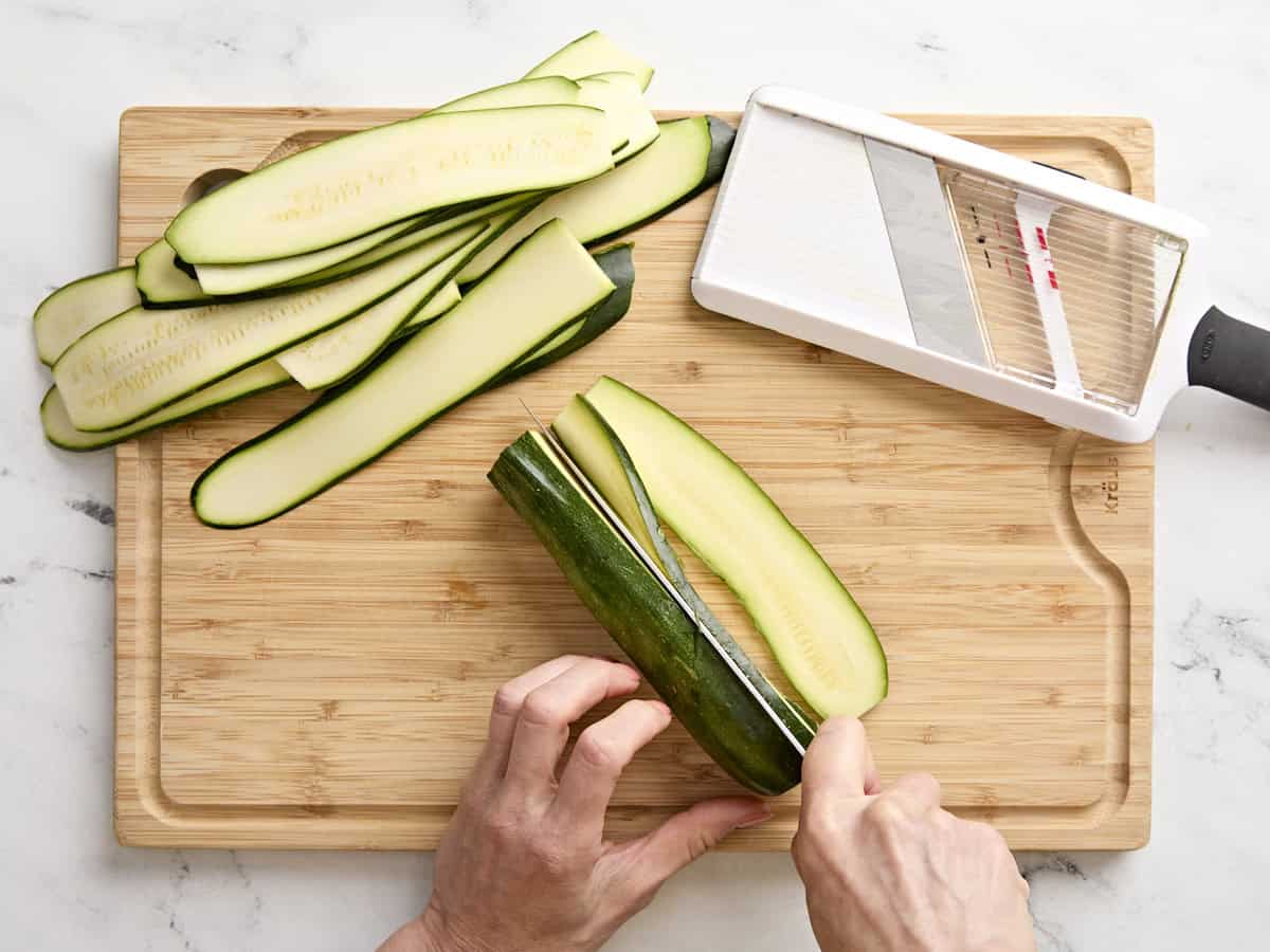 Zucchini being sliced on a wooden chopping board