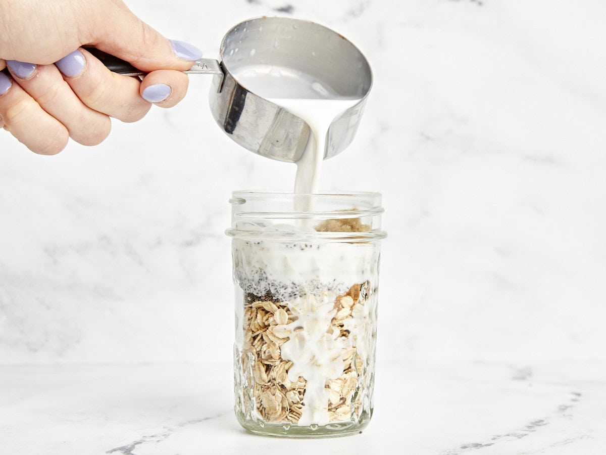 Ingredients for overnight oats in a mason jar with milk being poured in