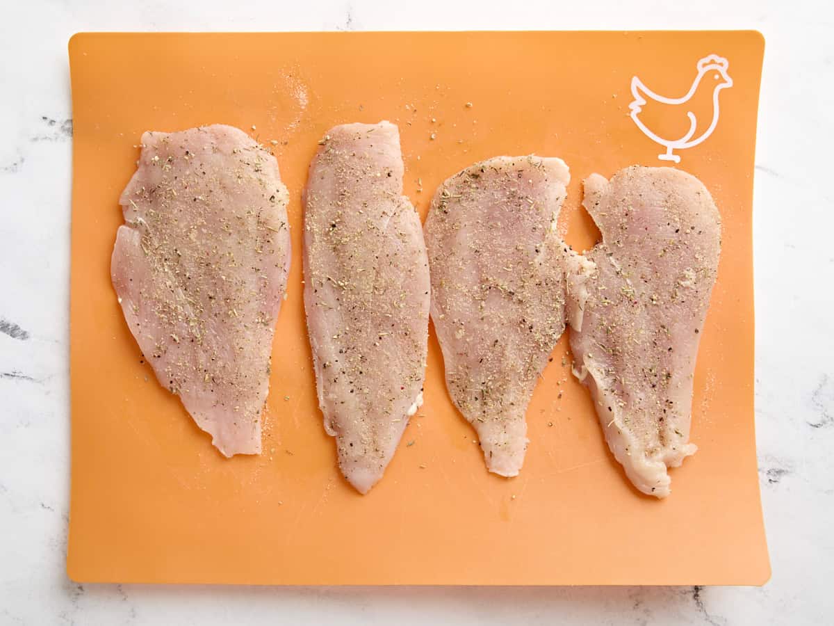 Seasoned chicken breasts on a cutting board.