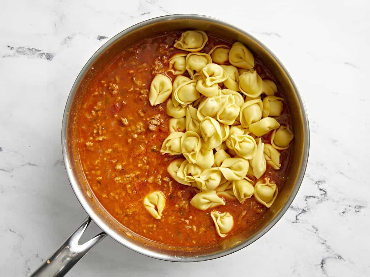 Cheese tortellini pasta added to sausage mixture in a skillet.