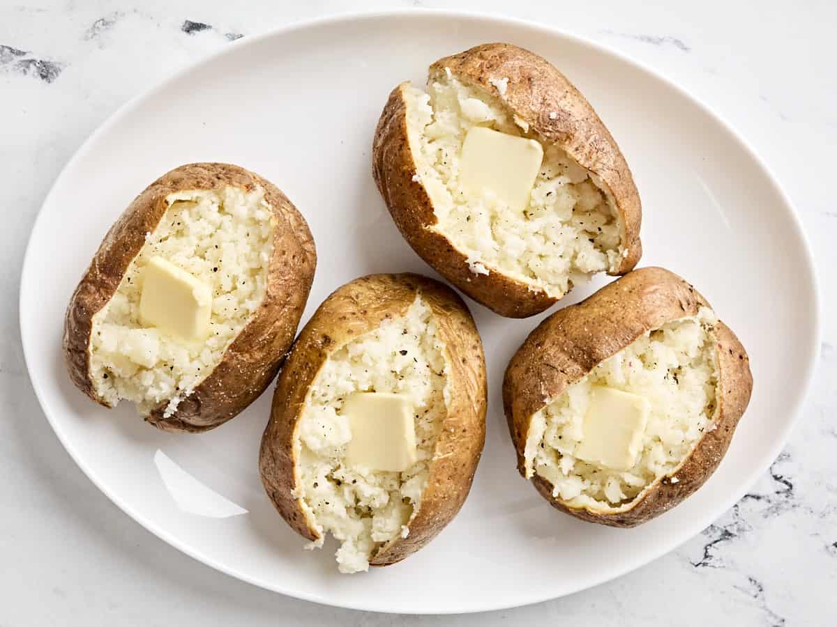 Four air fryer baked potatoes cut open with butter added on top.