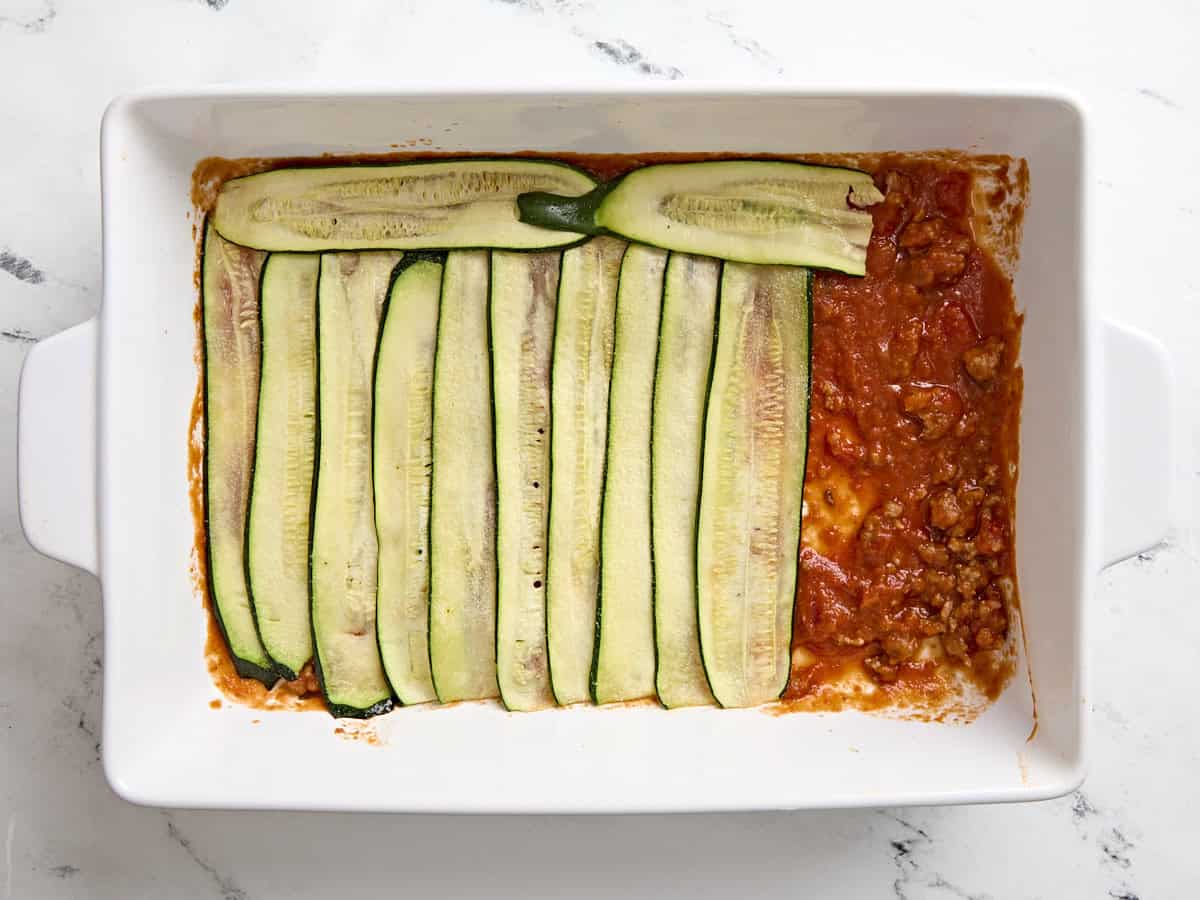 Layers of zucchini slices and sausage meat in a baking dish for zucchini lasagna