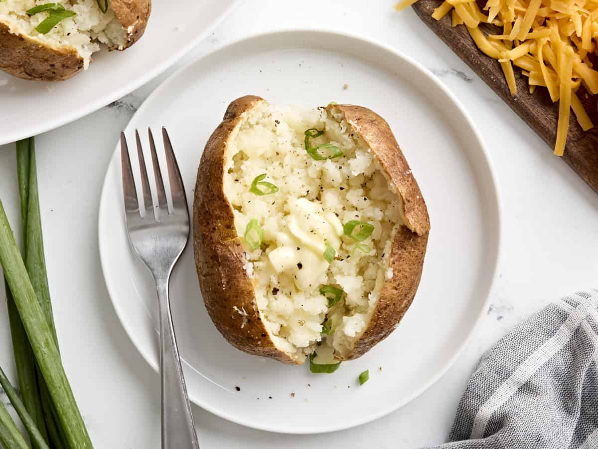 One air fryer baked potato on a white plate with a fork on the side.