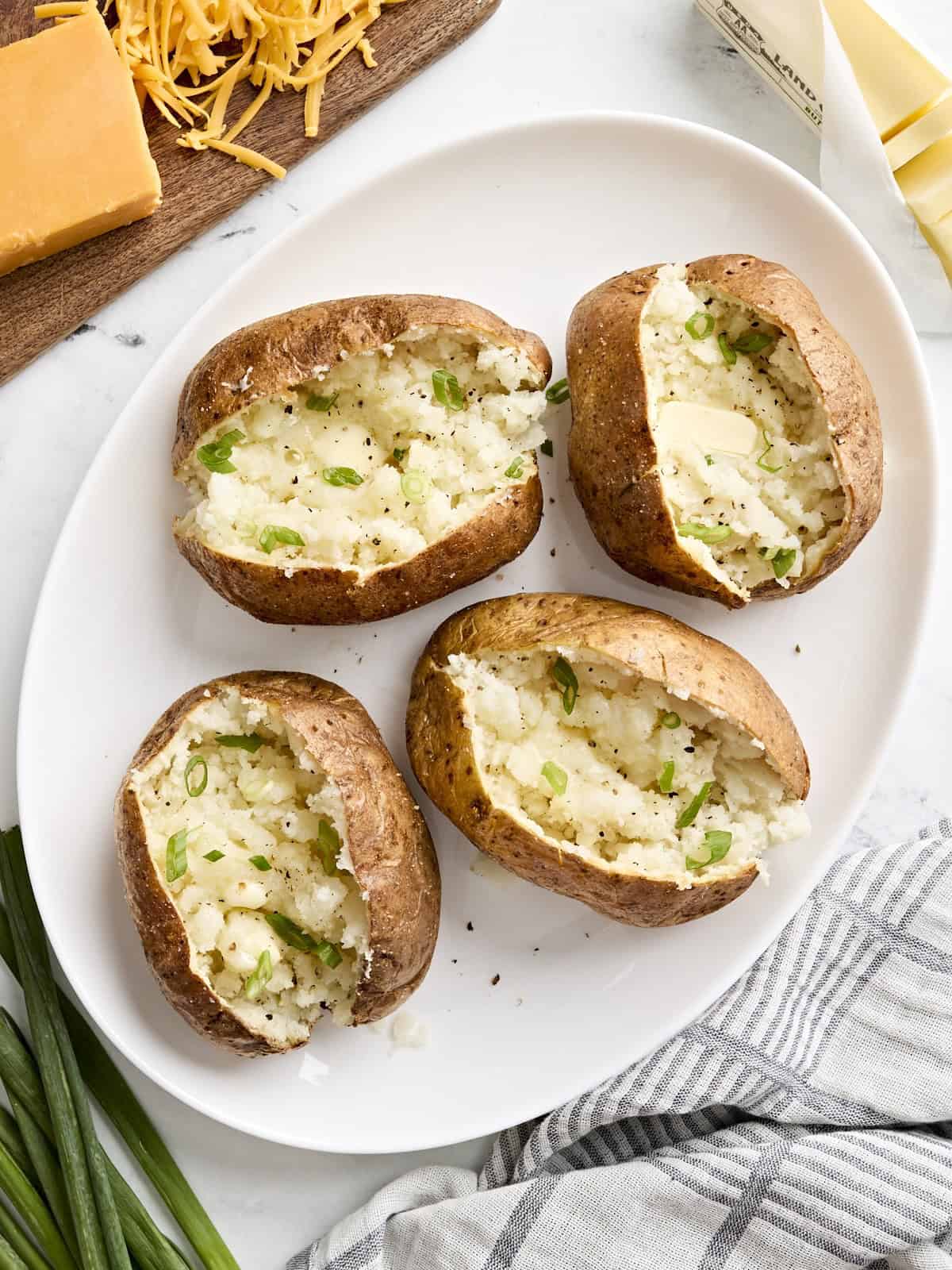 Overhead view of air fryer baked potatoes dressed with toppings on a white platter.