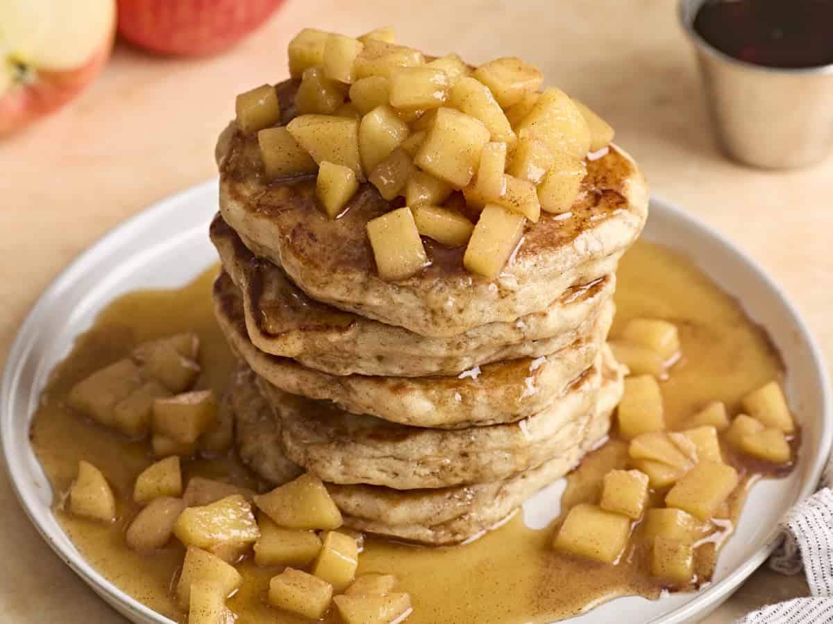 A stack of Apple Cinnamon Pancakes with maple syrup poured over the top.