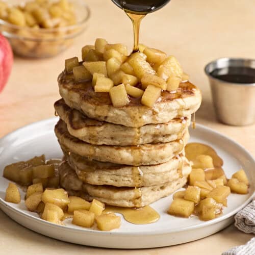 A stack of apple cinnamon pancakes with maple syrup being drizzled over top.