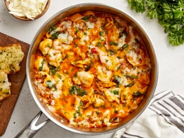 Overhead view of cheese tortellini and sausage skillet with garlic bread and parsley on the side.