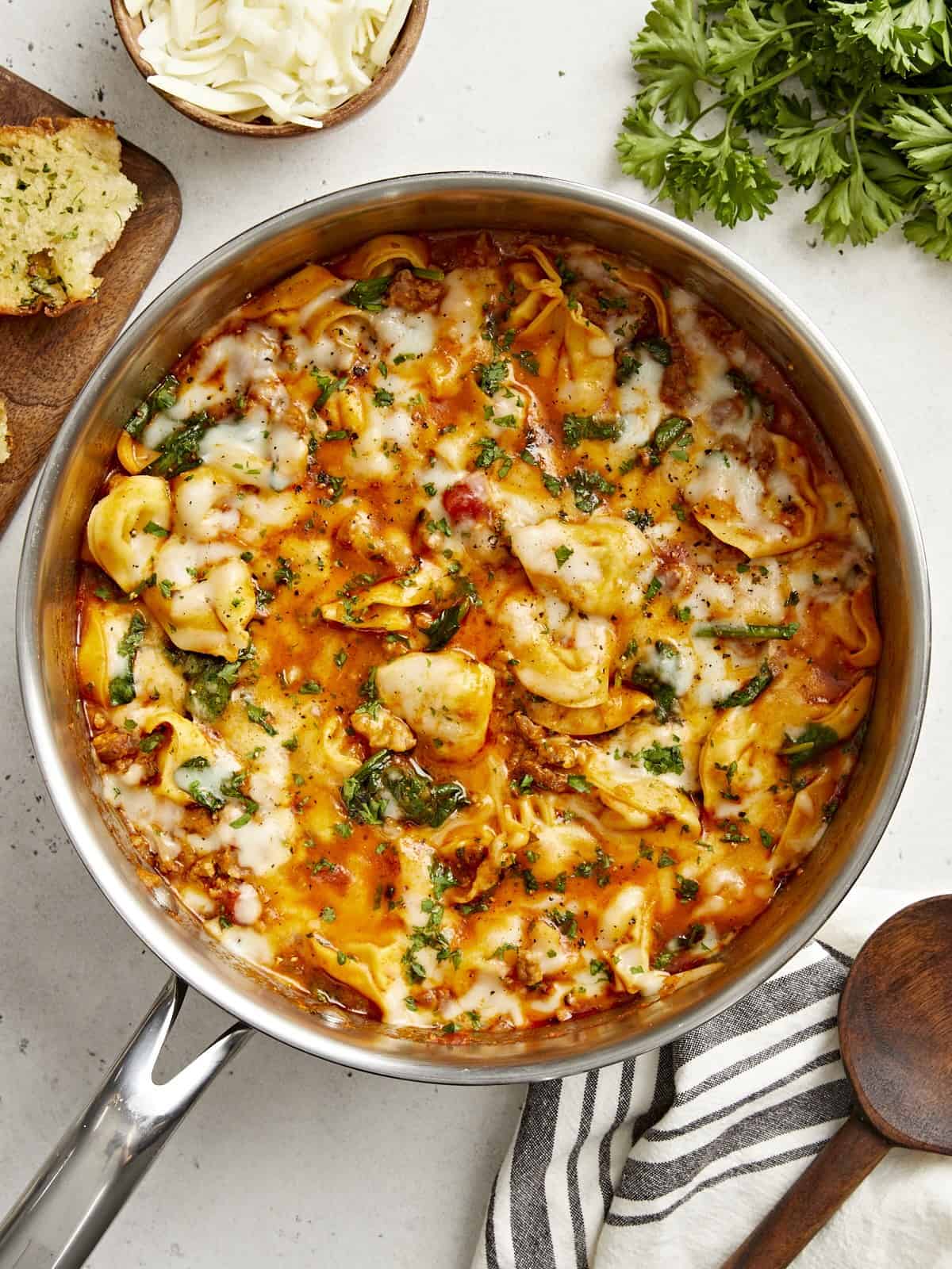 Overhead view of cheese tortellini and sausage skillet with garlic bread and parsley on the side.