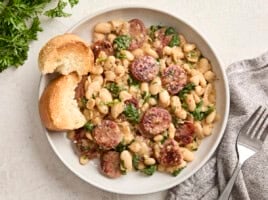 Overhead view of chicken sausage and white beans on a serving dish with toasted bread on the side.