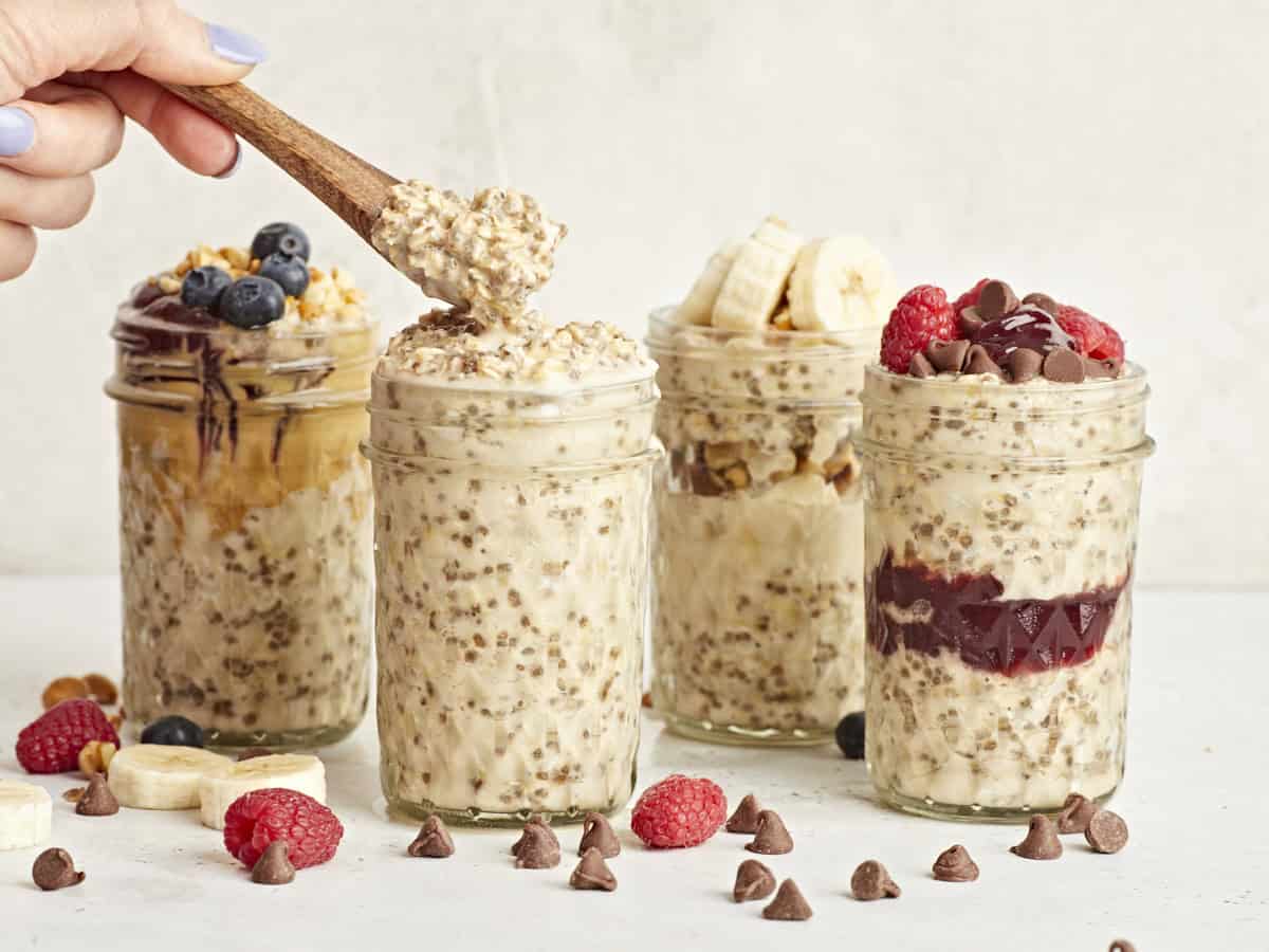 Side view of 4 jars of overnight oats with a wooden spoon taking some from one of the jars