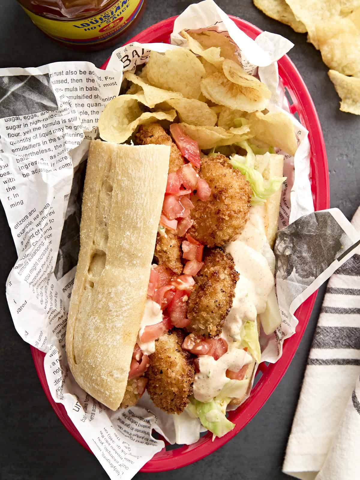 A shrimp po' boy in a basket with potato chips