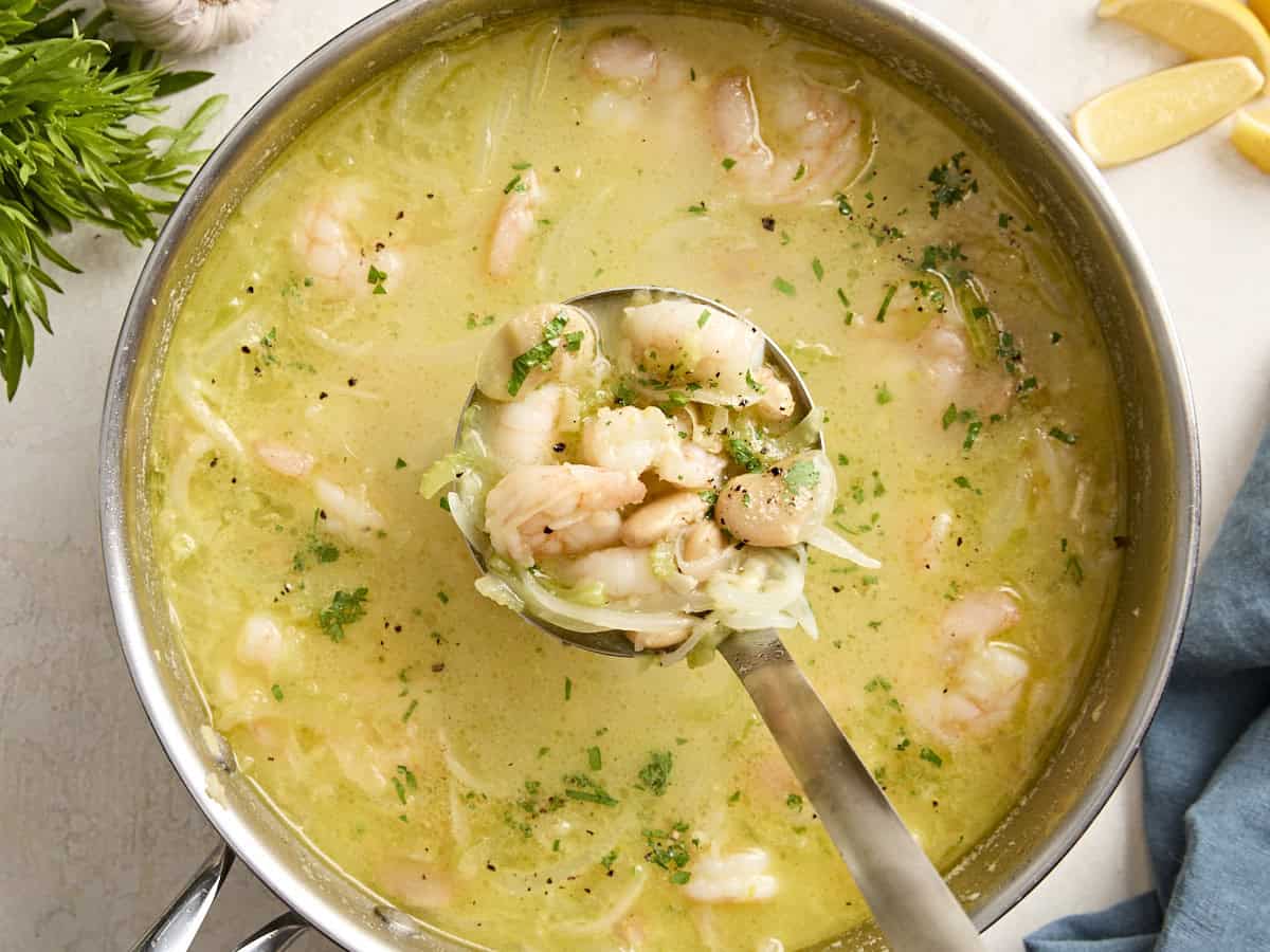 A ladle scooping some shrimp and white bean stew from a skillet