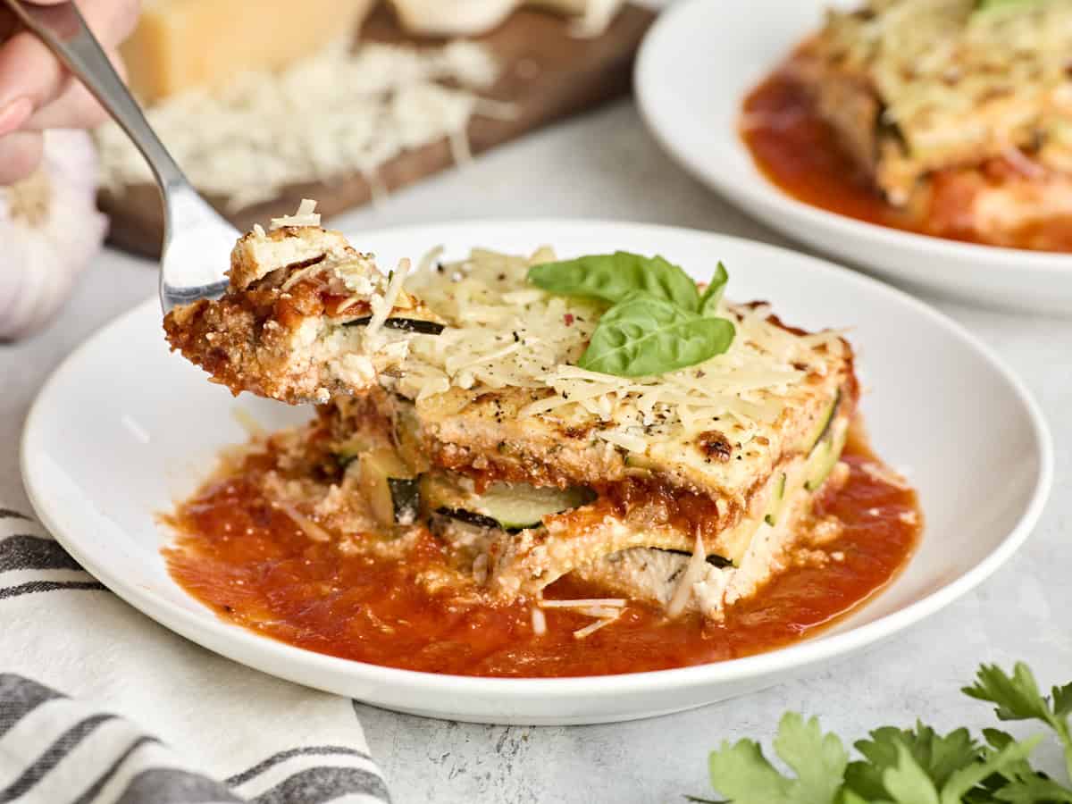 Side view of a slice of zucchini lasagna on a plate with a fork taking a piece