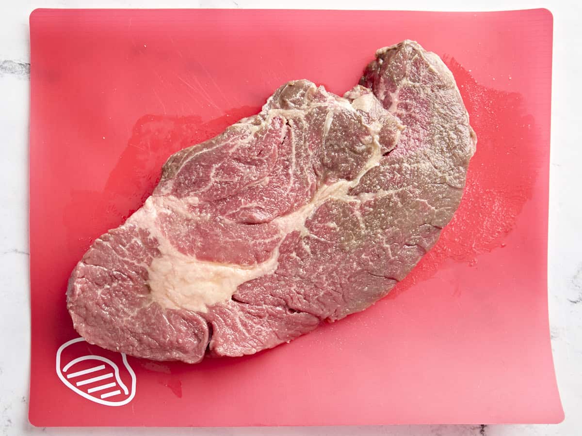 Raw chuck roast on a red meat mat.