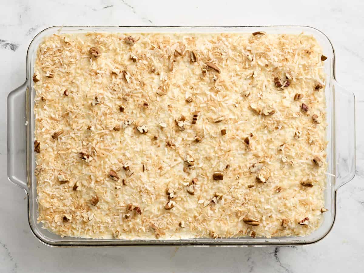 Do nothing cake topped with white frosting, toasted shredded coconut and chopped pecans in a baking dish.