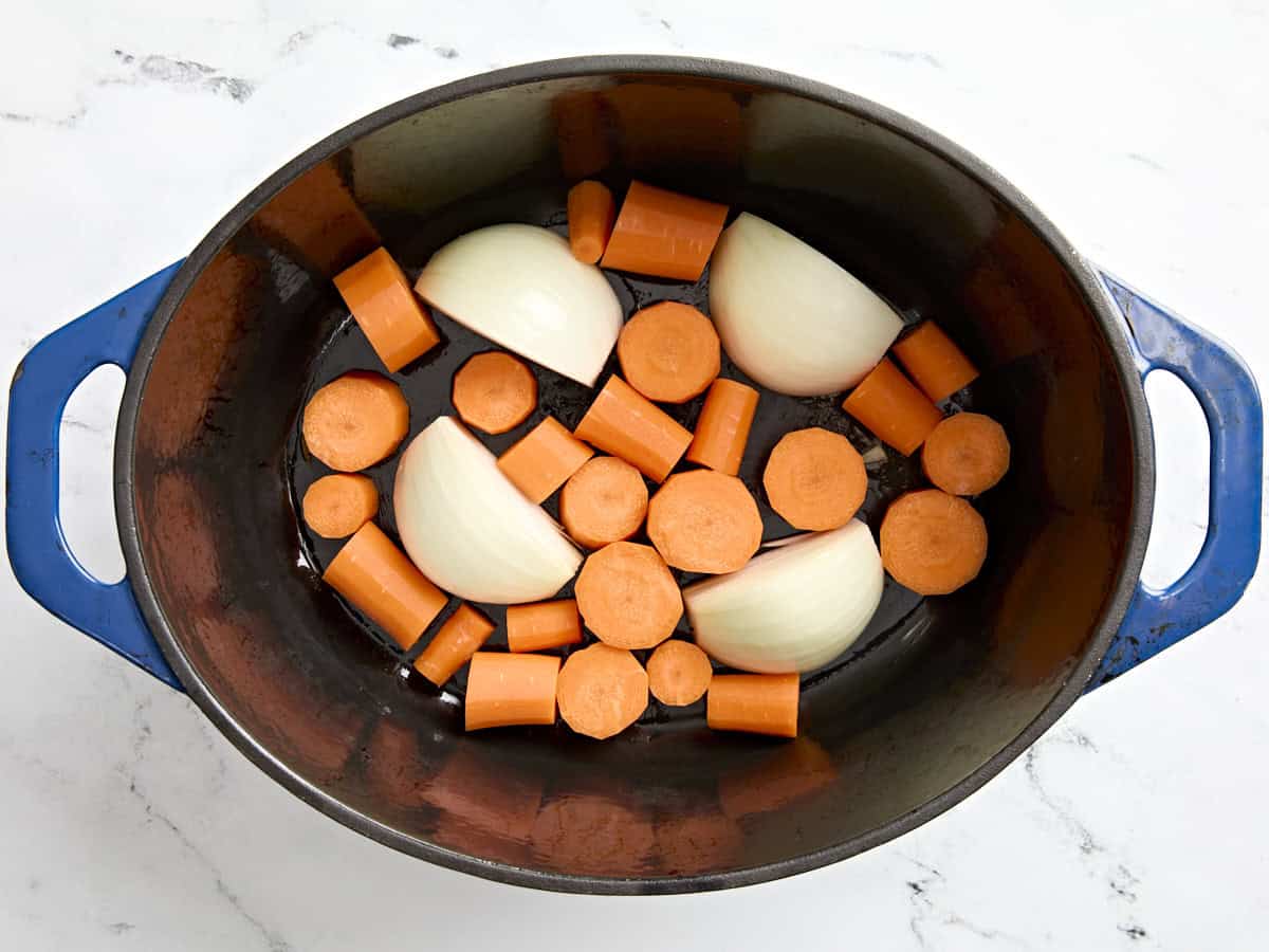 Sliced onions and carrots added to a dutch oven.