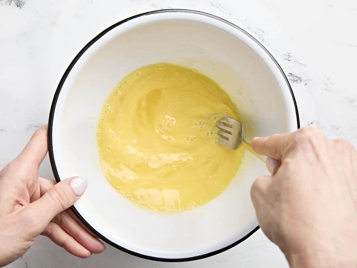 A fork whisking eggs in a mixing bowl.