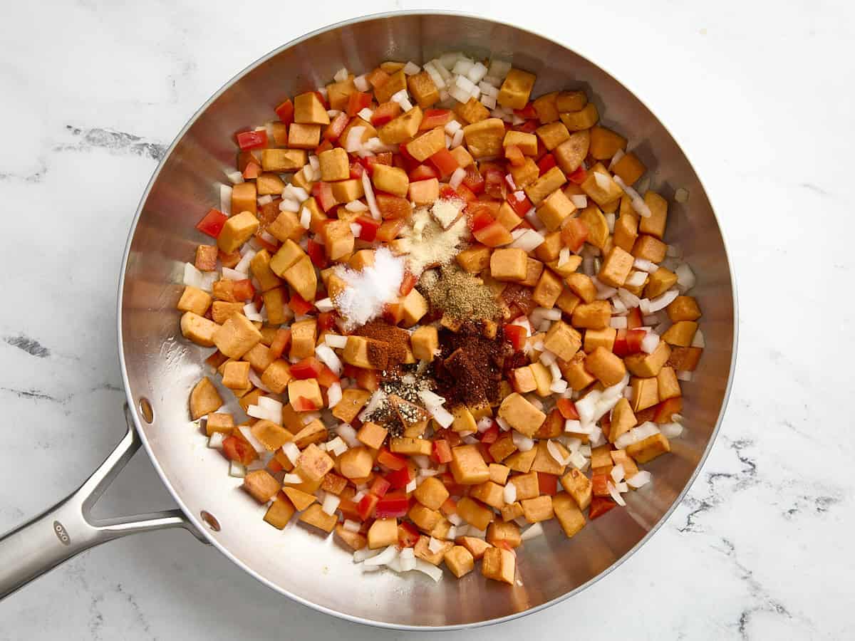 Spices added to sweet potatoes and veggies in a skillet.