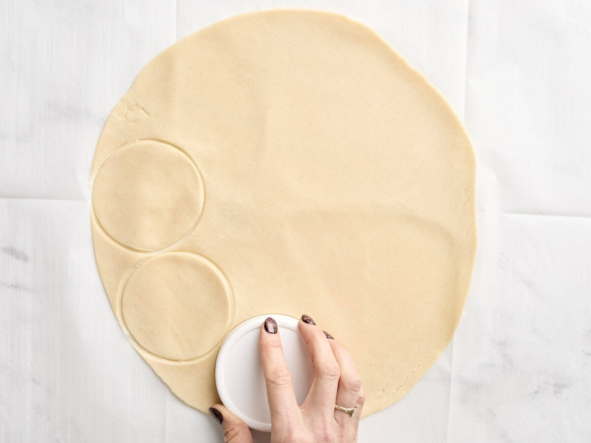 A hand cutting circles out of premade pie crust for butter tarts.