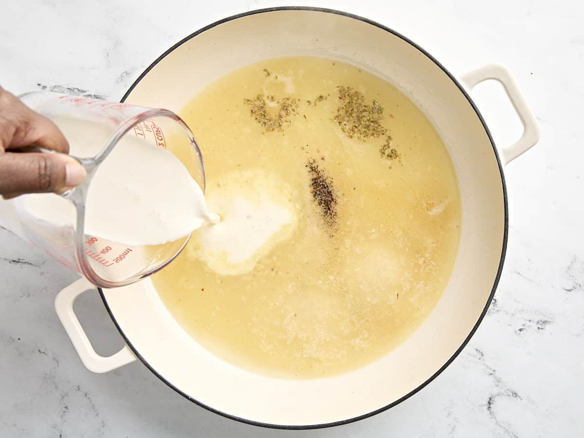 chicken broth, heavy cream, and spices being added to large skillet.