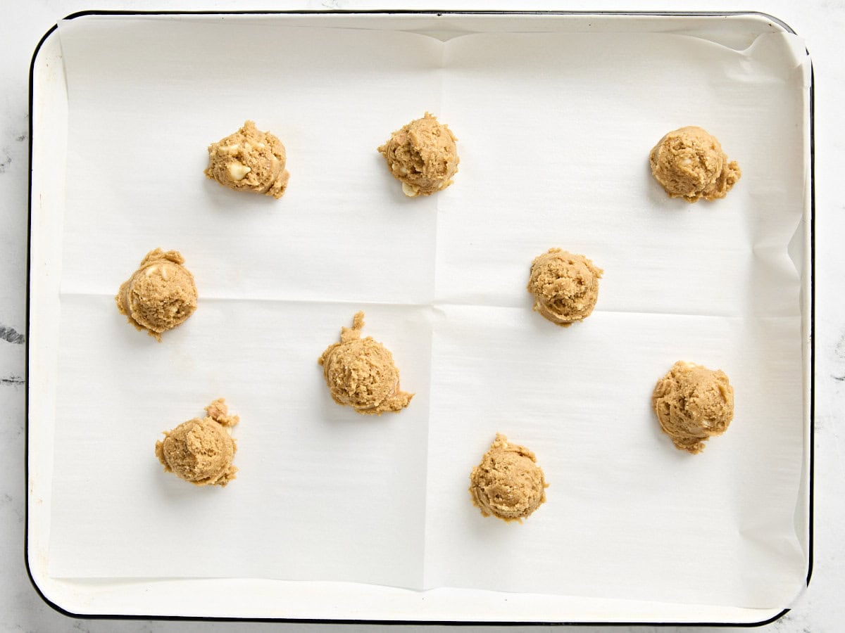 Balls of pumpkin cookie dough on a parchment lined baking sheet.