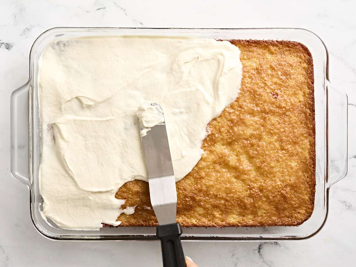 Do nothing cake being frosted with white frosting in a baking dish.