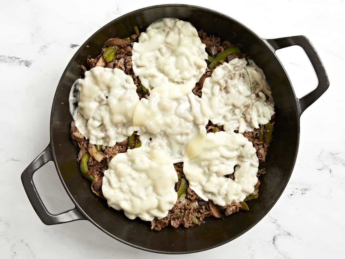 Provolone cheese added on top of cooked cheesesteak in skillet.