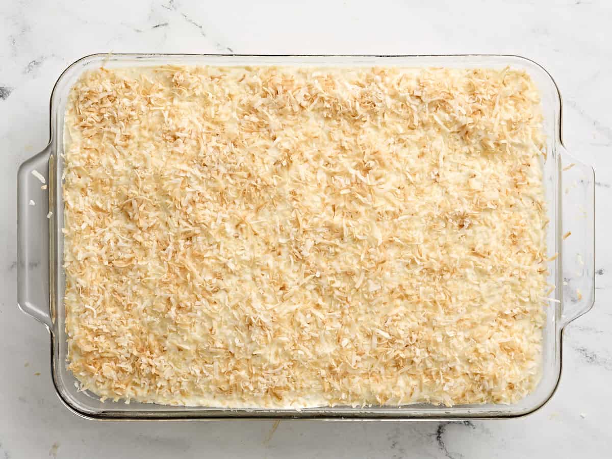 Frosted do nothing cake topped with toasted shredded coconut in a baking dish.