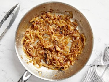 Overhead view of golden caramelized onions in a skillet, showcasing their rich color and glossy texture.