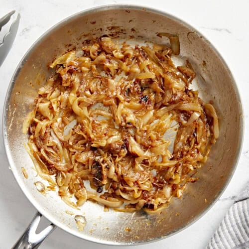 Overhead view of golden caramelized onions in a skillet, showcasing their rich color and glossy texture.