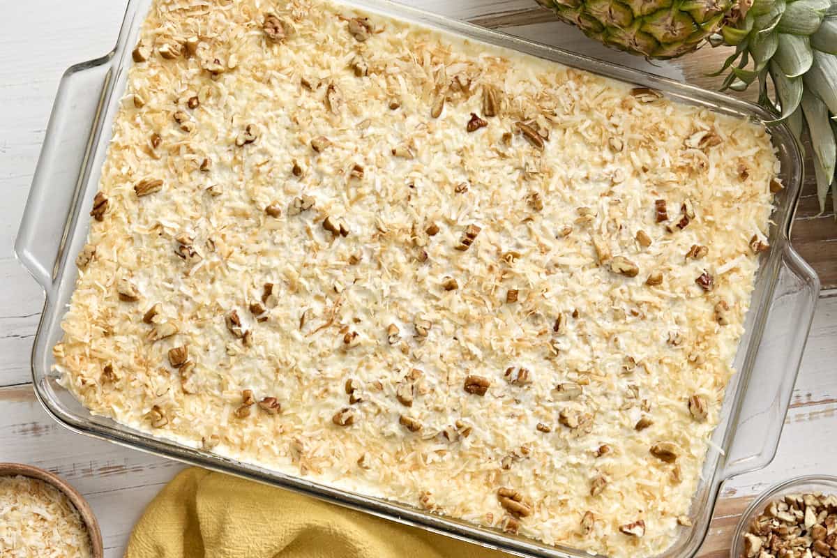 Do nothing cake topped with shredded coconut and chopped pecans in a baking dish.