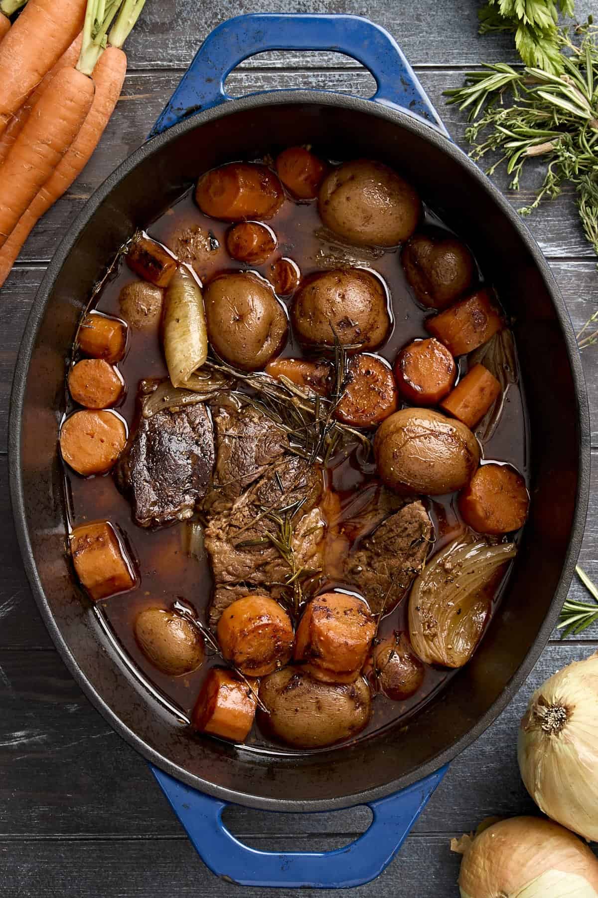 Pot roast in a dutch oven with potatoes, carrots, and onions.