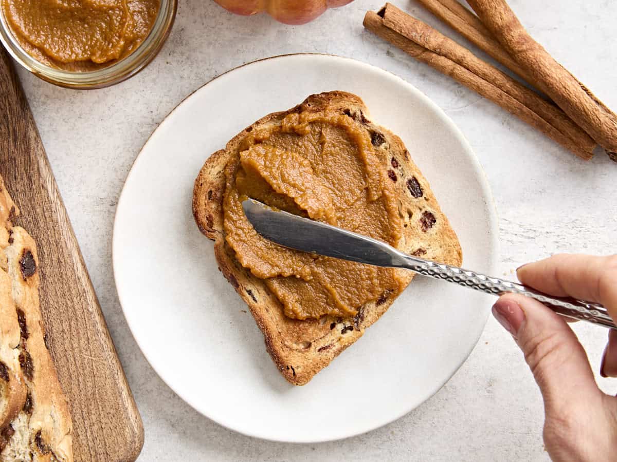 A knife spreading pumpkin butter onto a slice of raisin bread.