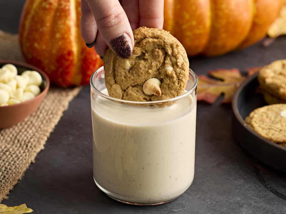 A hand dipping a pumpkin chip cookie into a glass of milk.