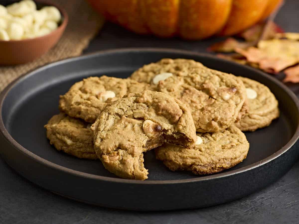 A plate of pumpkin cookies with one cookie missing a bite.