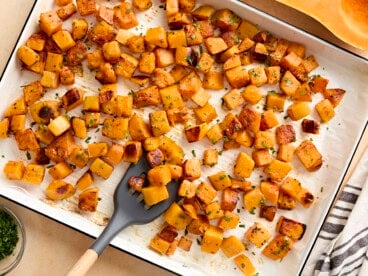 Overhead view of roasted butternut squash cubes on a baking tray with a spatula.