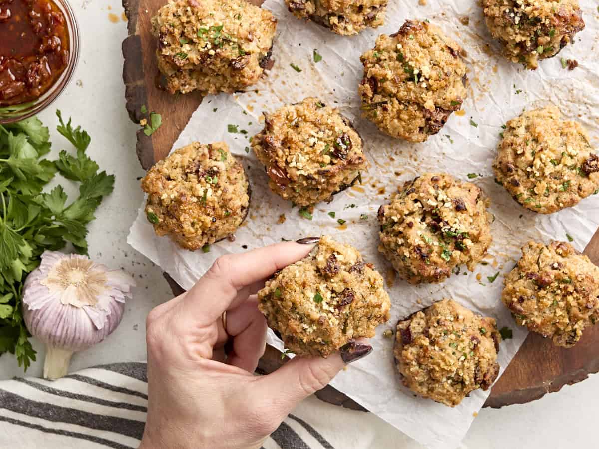 A hand taking a stuffed mushroom from a wooden chopping board.