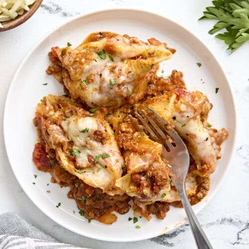 Overhead view of stuffed shells on a white plate with a fork cutting one of the shells in half.