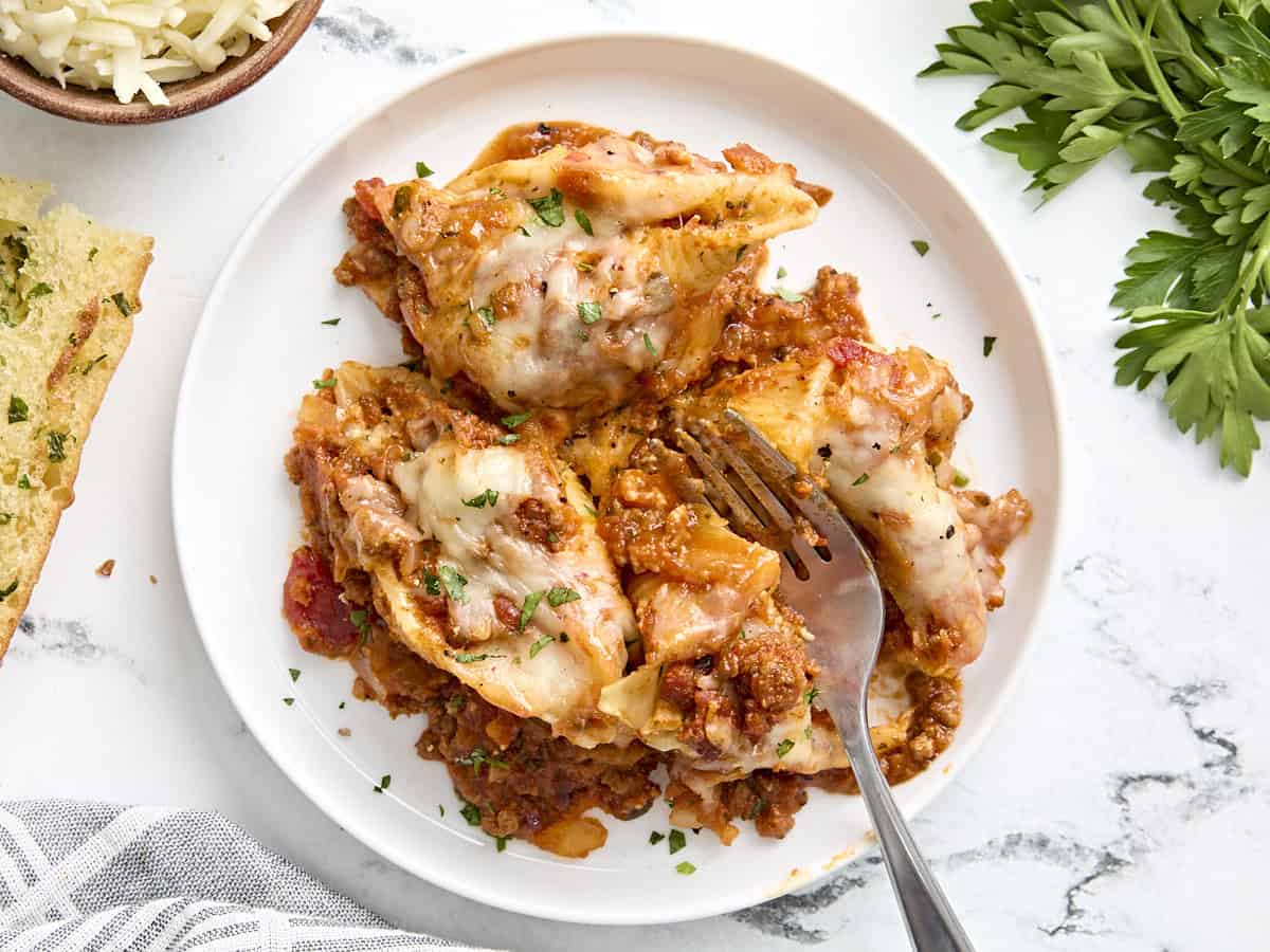 Overhead view of stuffed shells on a white plate with a fork cutting one of the shells in half.