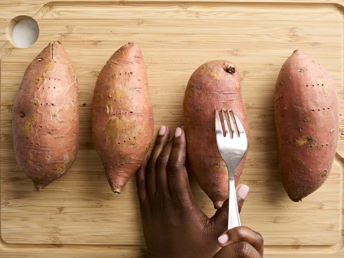 Poking 4 sweet potatoes with a fork.