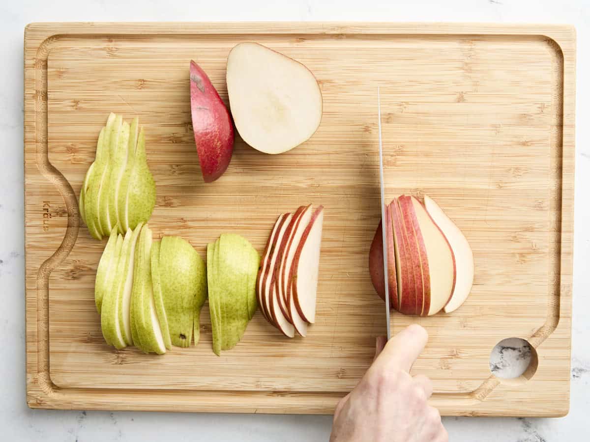 A knife slicing pears on a wooden chopping board.