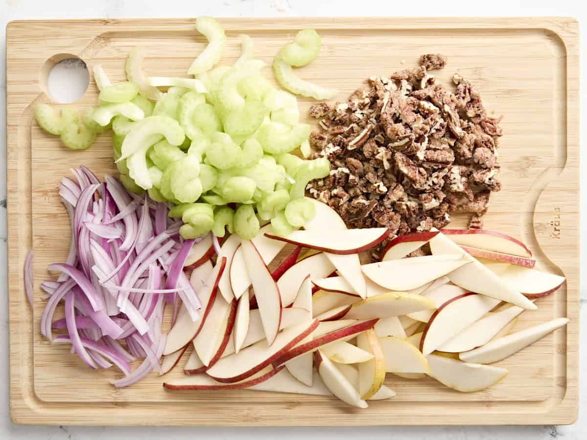 Diced candied pecans, celery, red onion, and pears on a wooden chopping board.