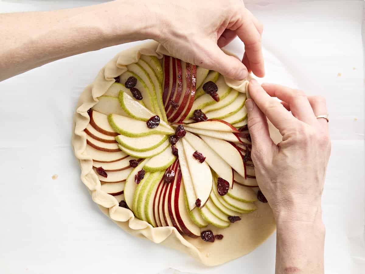 Hands folding and crimping the edges of a pear galette before baking.