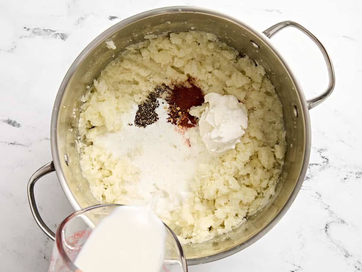 Seasonings, milk, and sour cream added to a pot with mashed potatoes.