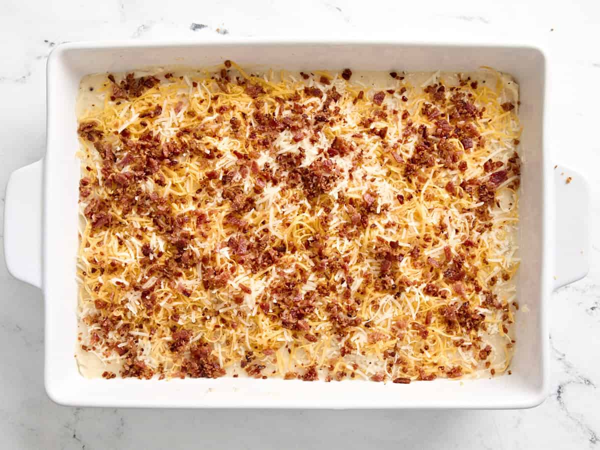 Mashed potato casserole topped with shredded cheese and bacon crumbles in a baking dish.