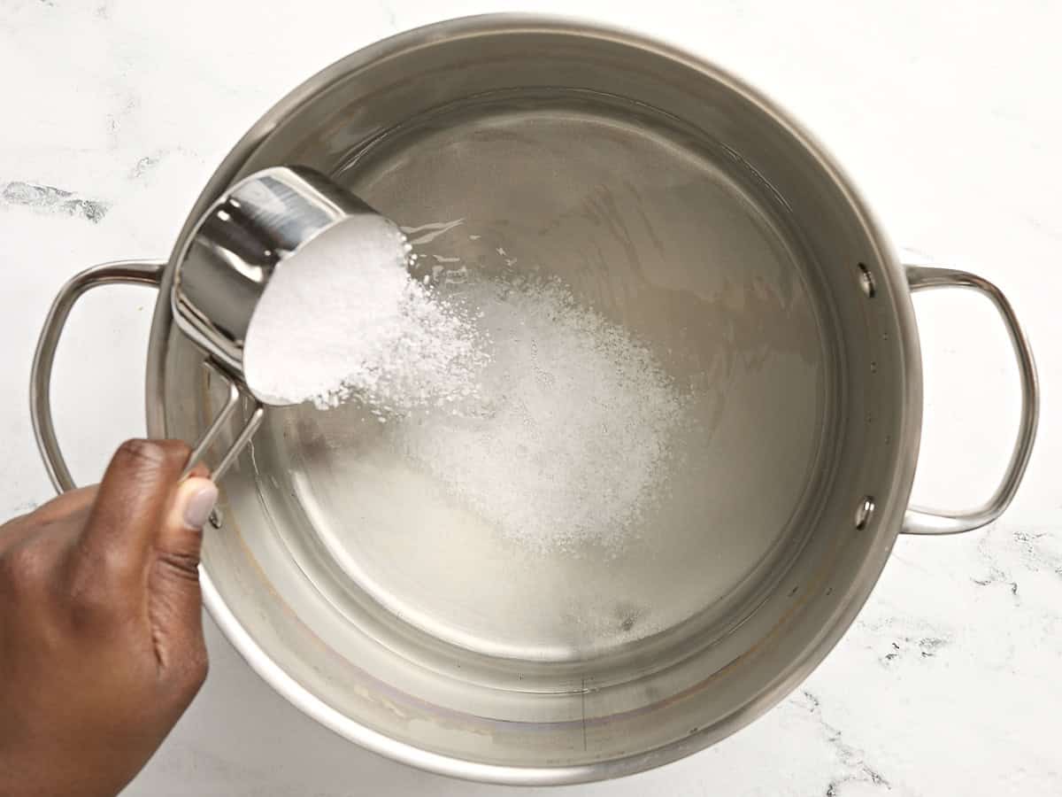 Salt and sugar being added to a large pot of water.