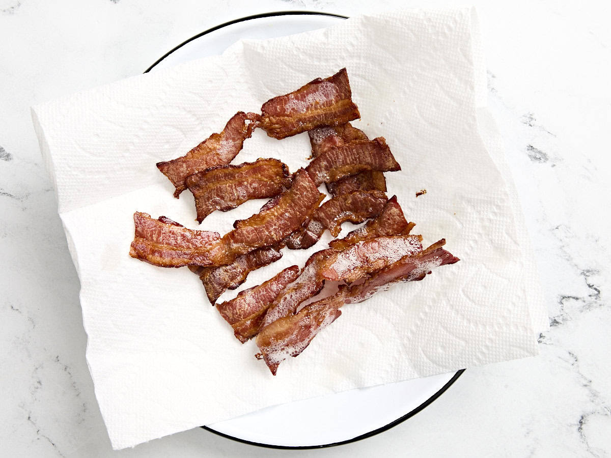 Crispy cooked bacon on a paper towel lined plate.