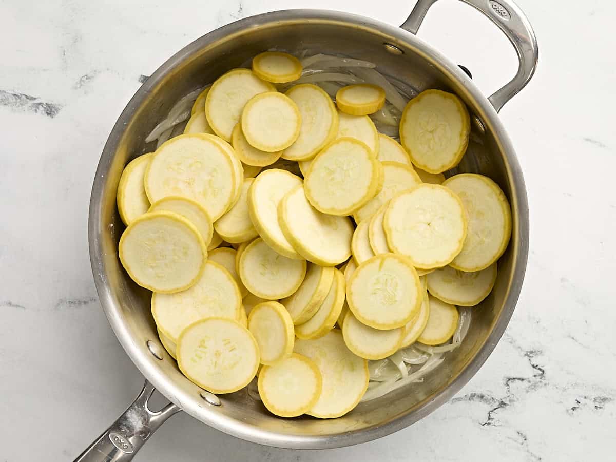 Sliced yellow squash cooking in a skillet with onions.