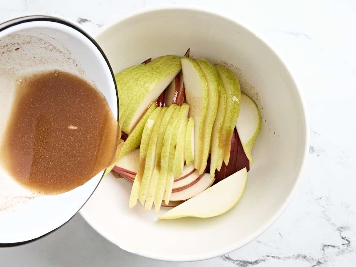 Spice mixture being poured over sliced pears in a mixing bowl.